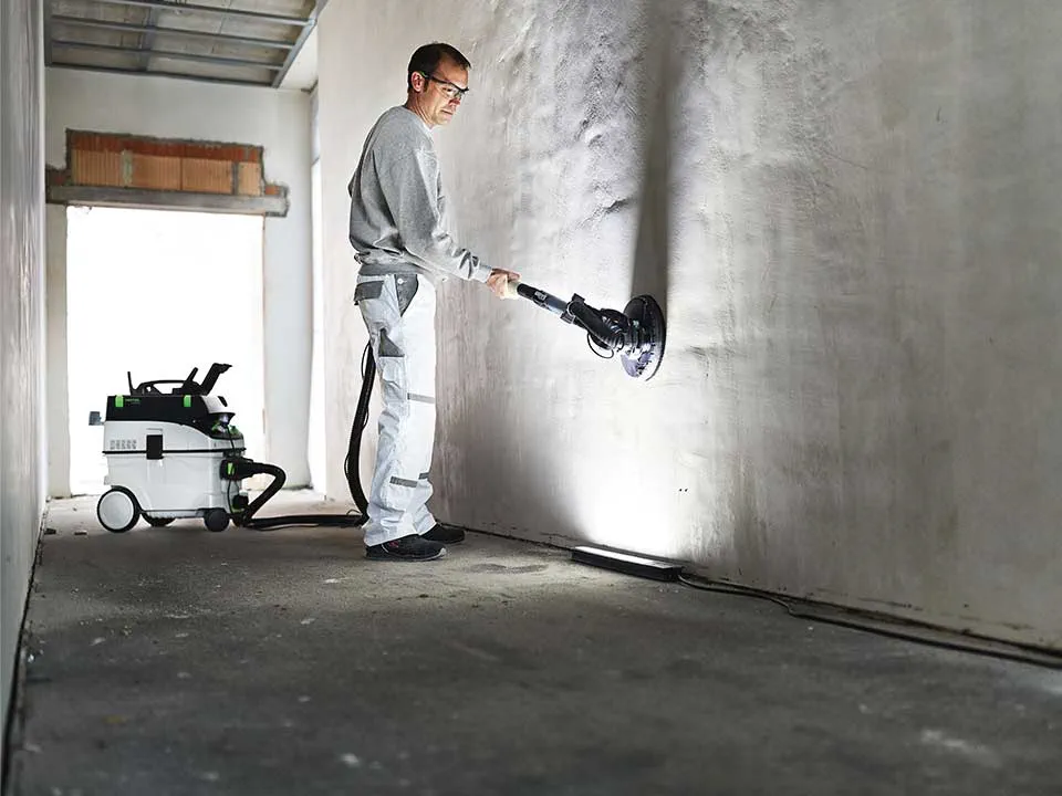 Rzemieślnik oświetla ścianę przy pomocy lampy kontrolnej i szlifuje ją.