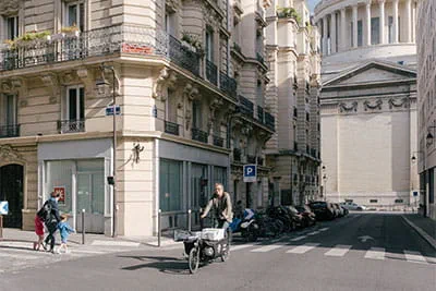W drodze do klienta „ébéniste à vélo” przejeżdża płynnie przez ruchliwe centrum Paryża na swoim rowerze towarowym, w tle słynna kopuła Panteonu.